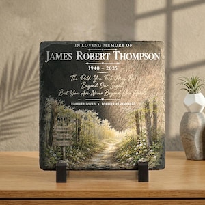 May include: A square slate memorial plaque featuring the text IN LOVING MEMORY OF JAMES ROBERT THOMPSON 1940-2025, The Path You Took May Be Beyond Our Sight, But You Are Never Beyond Our Hearts, FOREVER LOVED FOREVER REMEMBERED, and a forest path.