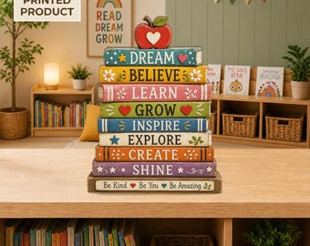 May include: A stack of nine rectangular blocks designed to look like books, topped with a red apple. Each block features a different color and word: DREAM, BELIEVE, LEARN, GROW, INSPIRE, EXPLORE, CREATE, SHINE, and Be Kind Be You Be Amazing.