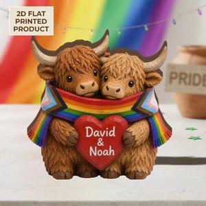Op de afbeelding: Een 2D plat gedrukt product met twee Hooglandrunderen die elkaar omarmen. Ze zijn gedrapeerd met een regenboog Pride-vlag en houden een rood hart met de namen "David & Noah" vast. De achtergrond bevat een regenboog en de tekst "2D FLAT PRINTED PRODUCT".