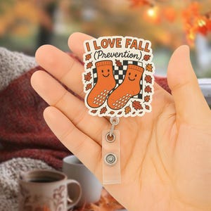 Może przedstawiać: Uchwyt na identyfikator z motywem jesiennym. Odznaka zawiera napis "I LOVE FALL (Prevention)" oraz dwie pomarańczowe skarpetki z uśmiechniętymi twarzami. Projekt otoczony jest jesiennymi liśćmi i czarno-białym szachownicowym tłem.