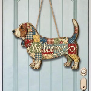 May include: Wooden basset hound-shaped welcome sign. The sign features a patchwork design in red, blue, yellow, and green. The word "Welcome" is written in cursive across the dog's body. The sign hangs from a jute rope.