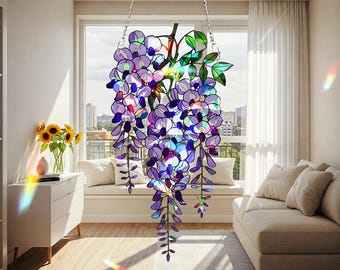 Peut inclure: Un panneau de glycine en vitrail suspendu à des chaînes devant une fenêtre. Le panneau présente des fleurs violettes et bleues avec des feuilles vertes. L'arrière-plan montre un paysage urbain et un canapé blanc.