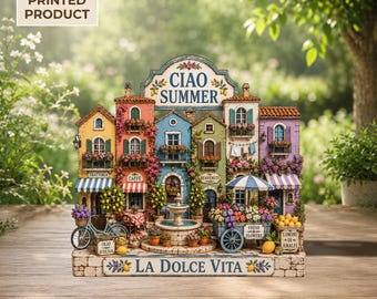 May include: A 2D flat printed decorative sign featuring a colorful Italian village scene with buildings, a central fountain, a bicycle, and a flower cart. The text reads CIAO SUMMER at the top and LA DOLCE VITA at the bottom, with various shop signs.