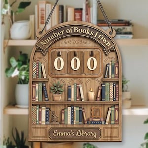 May include: Wooden sign with the text "Number of Books I Own" and "Emma's Library". The sign has a bookshelf design with a counter showing "000". Includes a small potted plant and a candle.