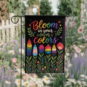 May include: A black garden flag with the text "Bloom in your own colors" in rainbow hues. The flag features colorful floral illustrations, including rainbow-colored flowers and green leaves, perfect for outdoor decor.