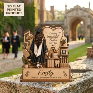 Pode incluir: Um presente de formatura em odontologia em madeira. Apresenta uma graduada com chapéu e toga, uma placa em forma de dente com o texto "Creating Beautiful Smiles Every Day" e uma base gravada com um nome e "Doctor of Dental Surgery - Class of 2026."
