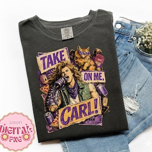 May include: A charcoal gray short-sleeve t-shirt featuring a graphic print of a long-haired person singing into a microphone with a cat wearing sunglasses. The text reads "TAKE ON ME, CARL!" surrounded by illustrations of pizza and soda cans.