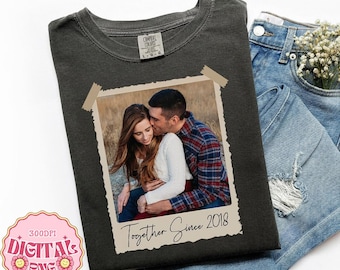 May include: A charcoal gray t-shirt featuring a rectangular photo print of a couple embracing, framed by beige tape graphics. The text "Together Since 2018" is printed in black script below the photo. The shirt has a crew neckline.