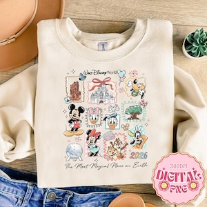 May include: Cream-colored sweatshirt featuring a colorful Disney World graphic. The design includes various Disney characters like Mickey Mouse, Minnie Mouse, and Goofy, along with the text "Walt Disney World" and "2026". The phrase "The Most Magical Place on Earth" is also present.
