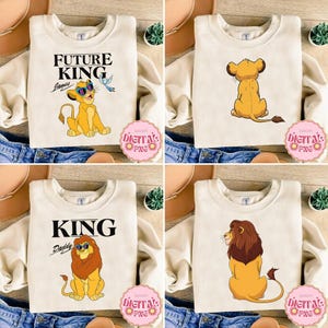Puede incluir: Cuatro sudaderas color crema con gráficos de leones. Una dice "FUTURE KING" con un cachorro de león con gafas de sol. Otra muestra un cachorro de león por la espalda. La tercera dice "KING Daddy" con un león con gafas de sol. La última muestra un león sentado.