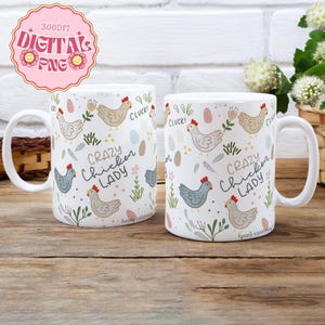 May include: Two white ceramic mugs with a chicken-themed design. The mugs feature illustrations of chickens, eggs, and floral elements, with the text "CRAZY Chicken LADY". The mugs are on a wooden surface.
