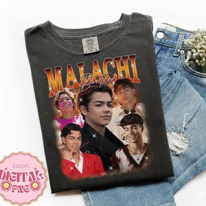 May include: Dark grey t-shirt with a collage of images of a young man, and the name "Malachi Barton" in orange and gold lettering. The shirt is displayed with blue denim shorts and a sprig of white flowers.