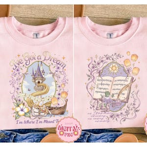 Op de afbeelding: Zachtroze sweatshirt met een sprookjesontwerp. De voorkant heeft de tekst "I've Got a Dream" en een kasteelillustratie. De achterkant heeft een muzieknotenontwerp. Het ontwerp bevat zwevende lantaarns en bloemelementen.