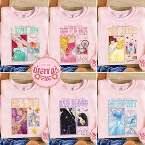 Può includere: Sei felpe rosa chiaro con grafiche a tema principesse. Ogni maglia presenta un design diverso con testi come "I LOVE HIM", "DREAMS" e "THE CURSE". I disegni includono illustrazioni di principesse e immagini correlate.