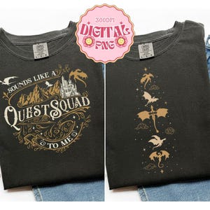 Op de afbeelding: Twee antracietgrijze T-shirts met goudkleurige afbeeldingen. Het linker T-shirt toont een kasteel, bergen en de tekst "SOUNDS LIKE A QUEST SQUAD TO ME". Het rechter T-shirt toont een verticale reeks van vliegende draak-silhouetten en sterren.