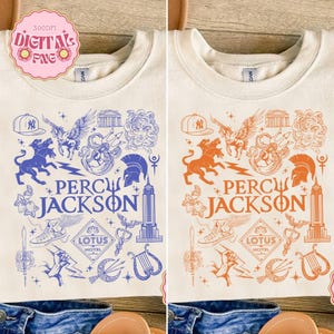 May include: Cream-colored t-shirt featuring a blue graphic design with the text "PERCY JACKSON." The design includes illustrations of a baseball cap, mythical creatures, and architectural elements. The shirt is displayed on a neutral background.