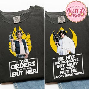 May include: Two dark gray t-shirts with Star Wars-themed graphics. One features Han Solo with the text "I take orders from no one but her." The other shows Princess Leia with the text "He has his moments, not many of them, but he does have them."