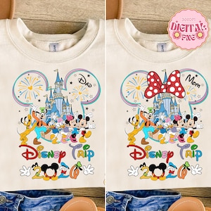 May include: Cream-colored t-shirts with a colorful Disney Trip 2020 design. One shirt features a Dad design, the other a Mom design with a red polka-dot bow. The design includes Disney characters, a castle, and fireworks.