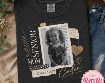 May include: A charcoal gray t-shirt featuring a collage-style graphic with a black and white photograph of a child, the text "SENIOR MOM" and "Class of 2027", a handwritten "Caden" script, floral line art, and two gold-colored heart icons.
