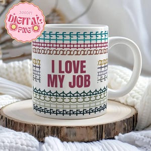Op de afbeelding: Witte keramische mok met de tekst "I LOVE MY JOB" in bordeauxrood. De mok heeft een decoratief patroon in teal, bordeauxrood, bruin en groen. De mok staat op een houten onderzetter.