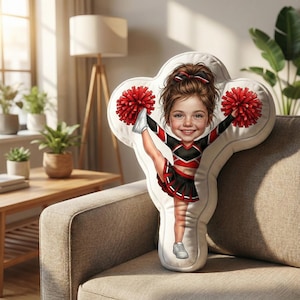 May include: A decorative pillow in the shape of a cheerleader. The pillow features a cartoon illustration of a girl in a red, black, and white cheerleading uniform, holding red pom-poms. The girl is smiling and has her leg extended in a split.