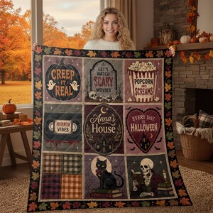 May include: A rectangular quilt featuring a grid of nine panels with Halloween-themed illustrations, including a pumpkin with the text 'CREEP IT REAL', a popcorn bucket labelled 'POPCORN AND SCREAMS', and a central panel reading 'Anna's House'.