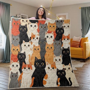 May include: A quilted blanket featuring a repeating pattern of cartoon cats in various colors, including black, orange, gray, and white. The cats have large eyes and are arranged in a grid-like design. The blanket is displayed indoors.