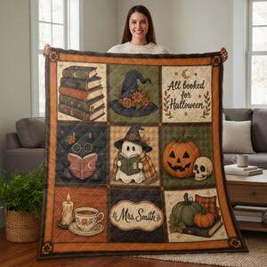 May include: A quilted throw blanket featuring a grid of nine Halloween-themed illustrations, including stacks of books, a witch hat, a black cat reading, a ghost, a jack-o'-lantern, a skull, a candle, a teacup, and the text All booked for Halloween.