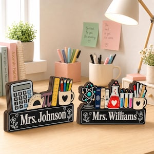 May include: Two personalized wooden desk signs with black bases featuring white text reading Mrs. Johnson and Mrs. Williams. The signs are decorated with colorful illustrations of school supplies, including a calculator, protractor, pi symbol, ruler, pencils, books, an atom model, and laboratory beakers.