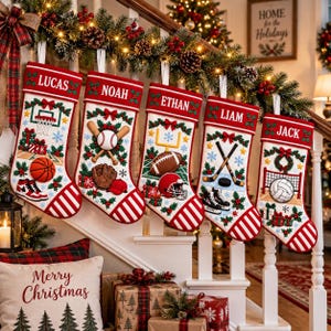 May include: Five white Christmas stockings with red cuffs and striped toes, each personalized with names Lucas, Noah, Ethan, Liam, and Jack. The stockings feature embroidered sports themes including basketball, baseball, football, hockey, and volleyball.
