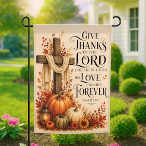 May include: A rectangular garden flag featuring a wooden cross draped in white fabric, surrounded by autumn leaves, berries, and three pumpkins. The text reads: Give Thanks to the Lord for He is Good His Love Endures Forever Psalm 136:1.