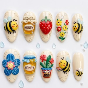 May include: A set of ten artificial nails with various 3D designs. The designs include a smiling bee, a jar of honey, a red strawberry, colorful flowers, and a blue flower. The nails are beige with small, dotted accents.