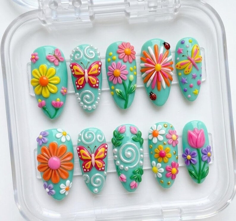 May include: A set of ten almond-shaped press-on nails with a light teal base, featuring 3D raised designs including colorful butterflies, various flowers like daisies and tulips, white swirls, small ladybugs, and tiny yellow stars.