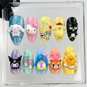 Może przedstawiać: Zestaw dziesięciu migdałowych paznokci typu press-on z figurkami 3D Sanrio. Wzory obejmują Cinnamoroll na niebieskim brokacie, Hello Kitty na różu, żółty paznokieć z gwiazdkami, Pompompurin, Badtz-Maru, Kuromi na fioletowym brokacie, Little Twin Stars, Tuxedosam, czerwoną pandę i Gudetamę na żółtym jajku.