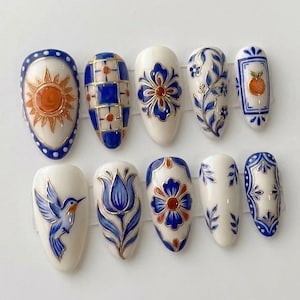 May include: A set of ten almond-shaped press-on nails featuring a cream-coloured base with intricate hand-painted designs in royal blue and orange. Patterns include a sun, a checkered grid, floral motifs, a hummingbird, and a tulip illustration.