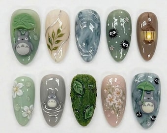 May include: A set of ten press-on nails featuring various designs including a grey character under a green leaf, botanical leaf art, blue marble swirls, soot sprites on sage green, a lantern, white flowers, and a character holding an umbrella.