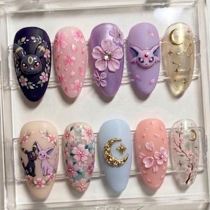 May include: A set of ten press-on nails featuring various designs including 3D sculpted characters, pink cherry blossoms, gold crescent moons, and celestial star patterns in shades of purple, pink, blue, and cream with glossy finishes.