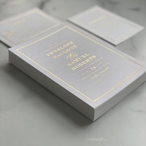 May include: A gray wedding invitation with gold foil lettering. The invitation reads "The Wedding of Penelope Saccone & Samuel Roberts Six o'clock in the evening June 14, 2023  Sockson & Branch Winery Napa Valley Reception to follow"