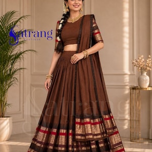 May include: A brown lehenga choli set featuring a solid brown cropped blouse and a matching pleated skirt. The skirt and the sleeves of the blouse are adorned with horizontal bands of black and metallic gold trim with thin red stripes.