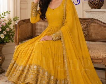 May include: A vibrant mustard yellow Anarkali dress featuring long sleeves with intricate gold embroidery, a matching dupatta, and a flared skirt with a wide, heavily embellished gold border. The garment includes subtle sequin detailing throughout.