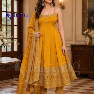 May include: A mustard yellow sleeveless Anarkali dress with thin straps, featuring intricate gold embroidery and mirror work along the neckline and hem. The outfit includes matching slim-fit trousers and a coordinating dupatta with a decorative border.