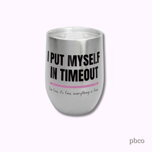 May include: A stainless steel wine tumbler with a lid. The tumbler has the phrase "I PUT MYSELF IN TIMEOUT" in black text, with a pink line underneath. Below the line, the text reads "I'm fine, it's fine, everything is fine."
