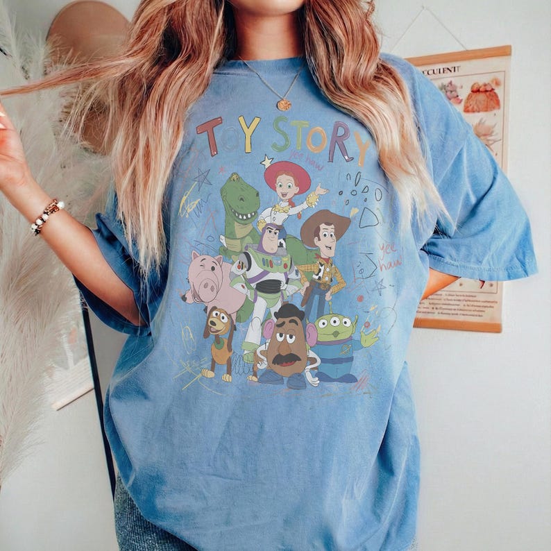 Puede incluir: Camiseta azul claro con un gr&aacute;fico de personajes de la pel&iacute;cula de animaci&oacute;n "Toy Story". El dise&ntilde;o incluye a Woody, Buzz Lightyear, Jessie y otros personajes. El texto "TY STORY" est&aacute; en la parte superior del gr&aacute;fico.