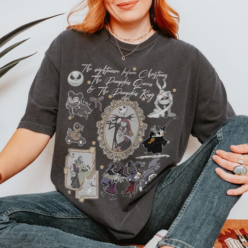 Pu&ograve; includere: T-shirt grigio scuro con personaggi e testo da "Nightmare Before Christmas". Il design include Jack Skellington, Sally e altri personaggi in stile vintage. Il testo recita "The Nightmare Before Christmas, The Pumpkin Queen & The Pumpkin King."