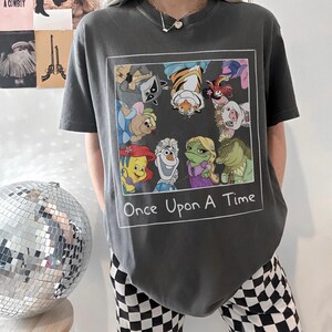 May include: Dark gray t-shirt featuring a framed graphic of cartoon characters, including a raccoon, tiger, and frog. The text "Once Upon A Time" is below the graphic. The shirt has short sleeves.