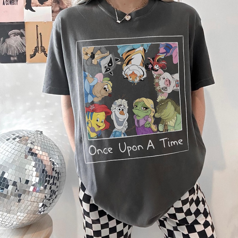 May include: Dark gray t-shirt featuring a framed graphic of cartoon characters, including a raccoon, tiger, and frog. The text "Once Upon A Time" is below the graphic. The shirt has short sleeves.
