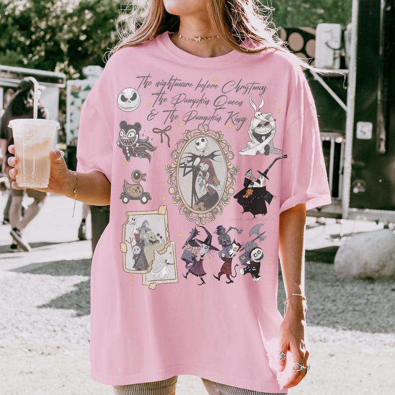 Pu&ograve; includere: T-shirt rosa chiaro con personaggi e testo di "Nightmare Before Christmas". Il design include Jack Skellington, Sally e altri personaggi iconici del film. Il testo recita "The Nightmare Before Christmas, The Pumpkin Queen & The Pumpkin King."