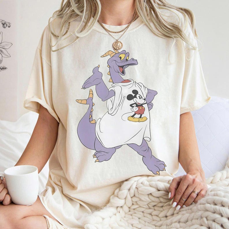 Peut inclure: T-shirt cr&egrave;me avec un dragon violet portant un t-shirt blanc avec un motif Mickey Mouse. Le dragon a des cornes et des griffes jaunes. Le t-shirt est de coupe ample.