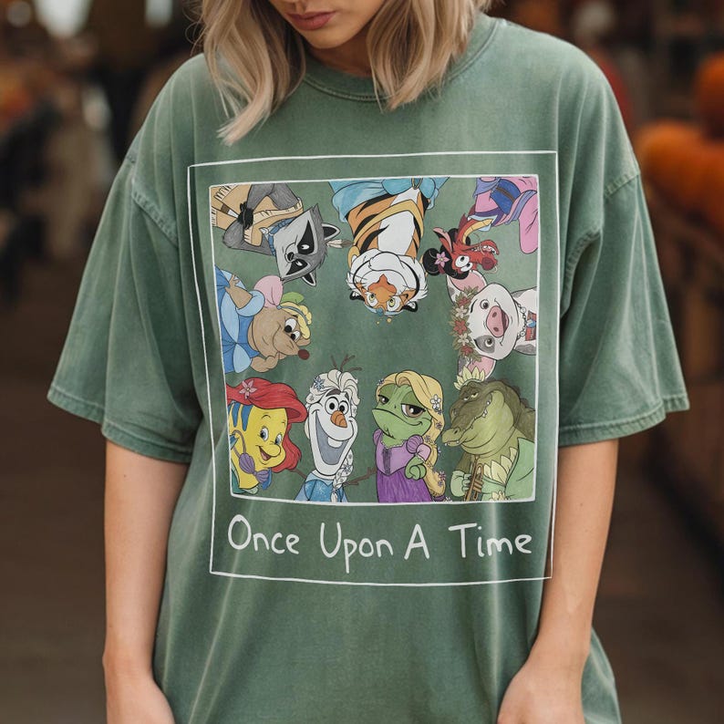 May include: Green t-shirt featuring a rectangular graphic with cartoon characters and the text "Once Upon A Time" in white. The graphic includes a raccoon, tiger, and other animated figures. The shirt has short sleeves and a relaxed fit.