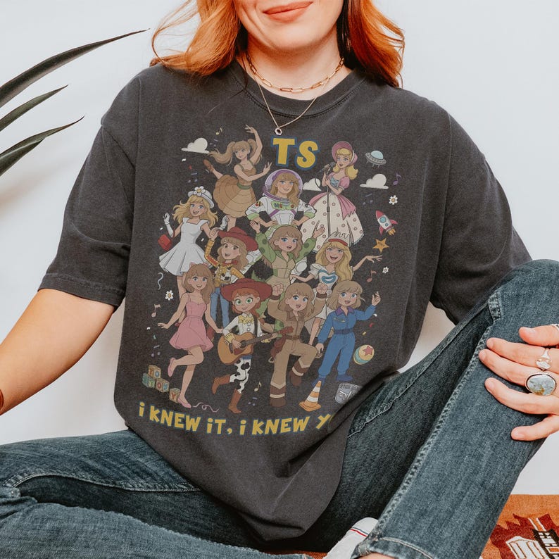 May include: A charcoal gray short-sleeve t-shirt featuring a graphic print of multiple animated characters in various outfits. The text TS is printed at the top, and the text i knew it, i knew you is printed at the bottom in yellow lettering.